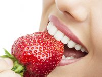 Extreme close up of teeth biting strawberry.